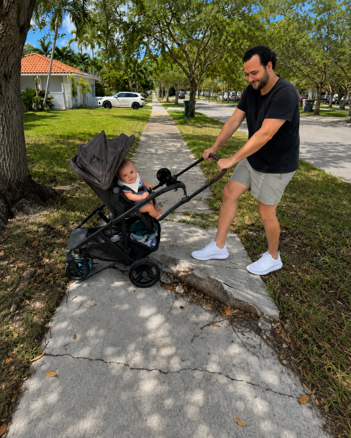 A father pushing a stroller stops at a slab of sidewalk lifted and cracked by a tree root