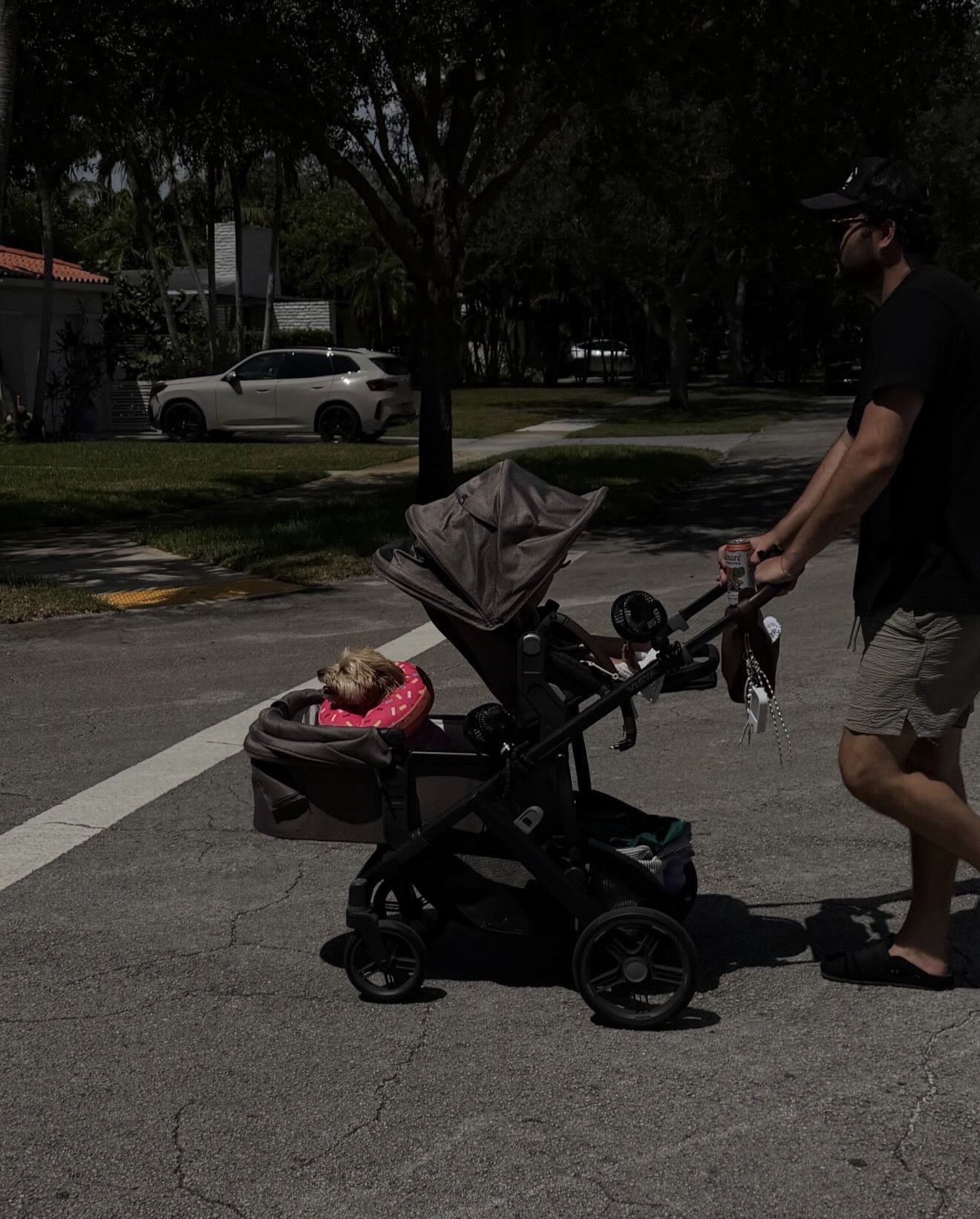 A father pushing a stroller in the street rather than on the sidewalk